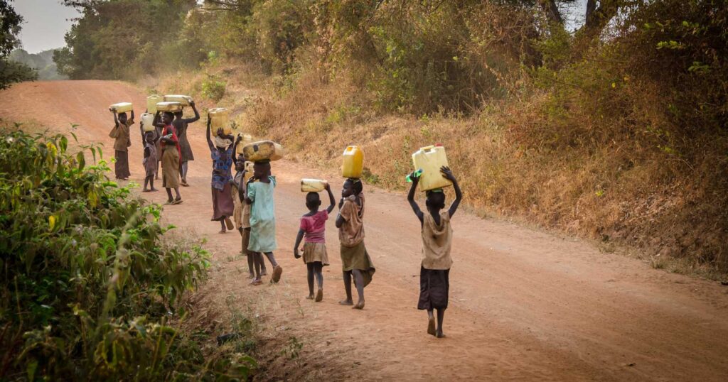 A group of children in Africa carrying water in cannisters over their head across a road