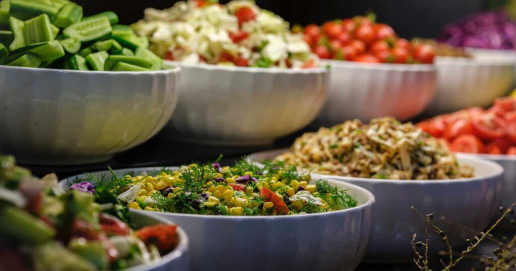 A line of large white bowls with healthy vegan food at a buffet.